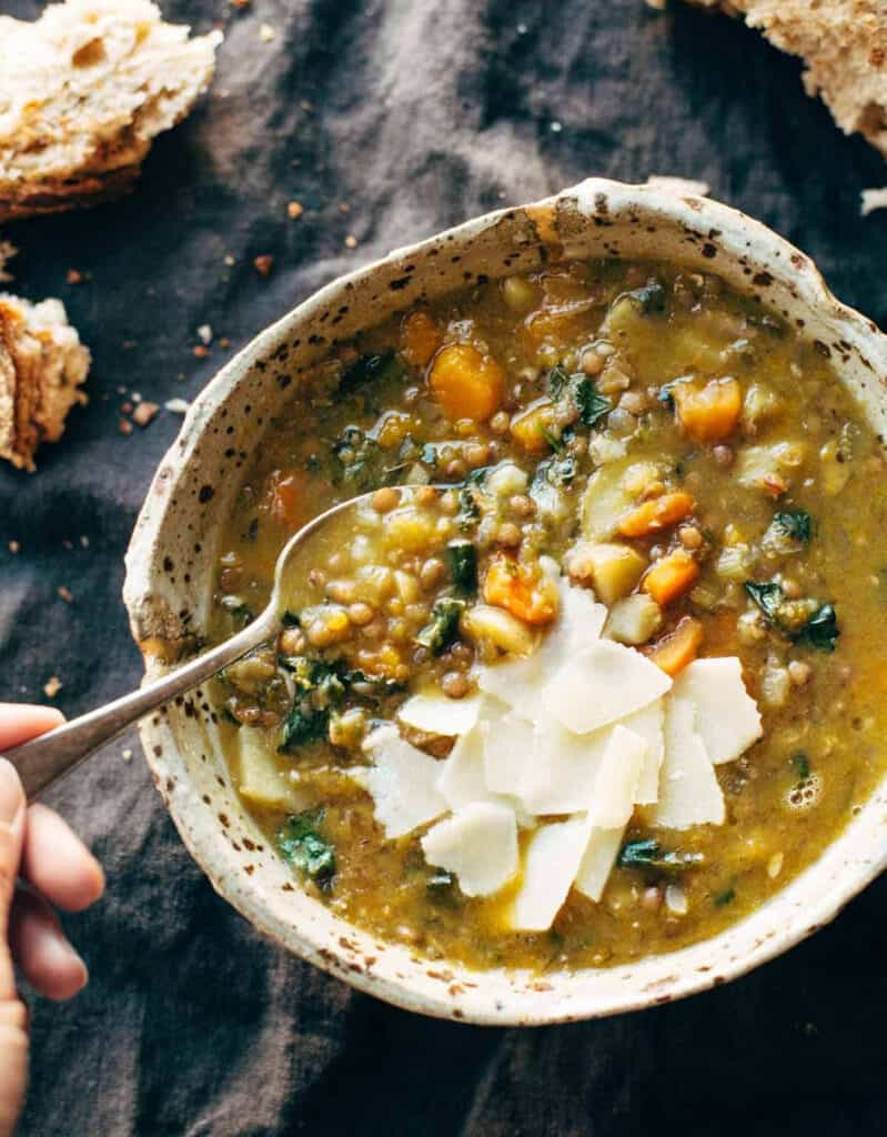 Top view of a rustic bowl with green lentil soup and a spoon over a dark background.