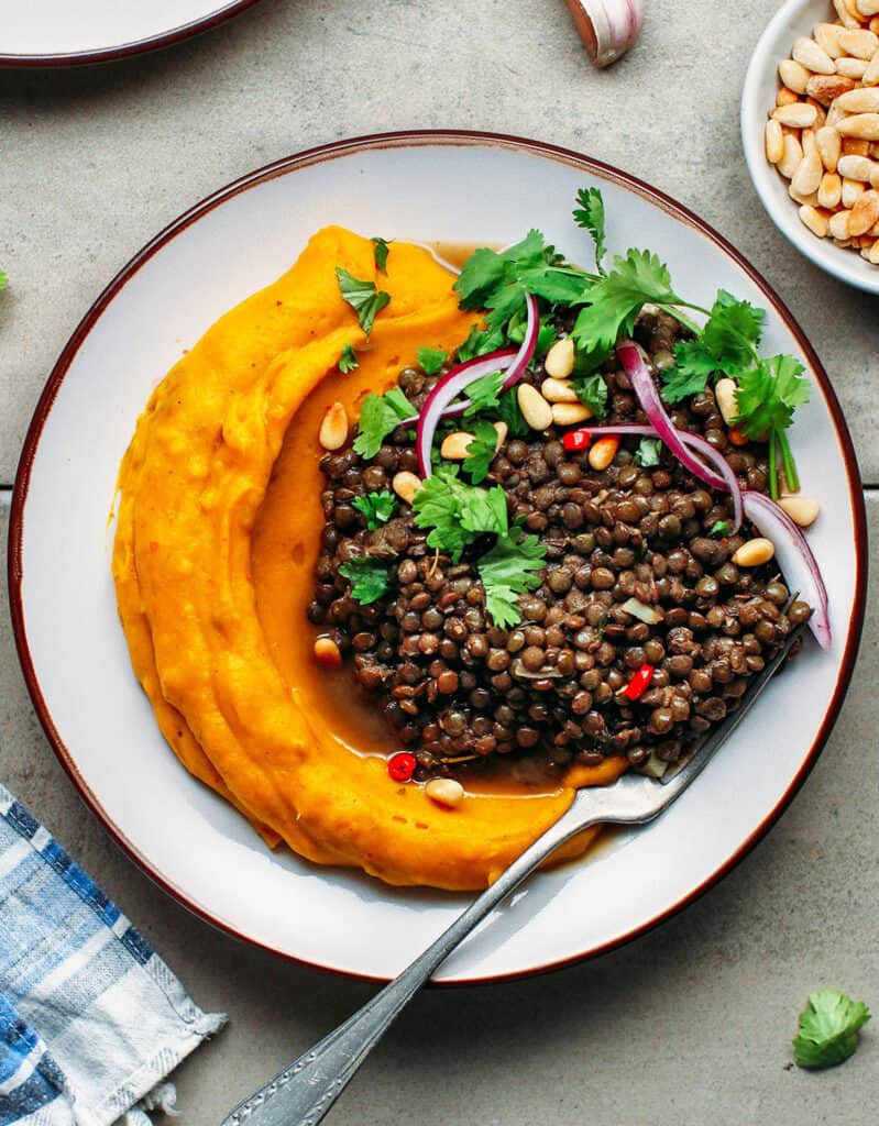 Top view of another green lentil recipe with a plate full of mashed pumpkin and lentils over a grey background.