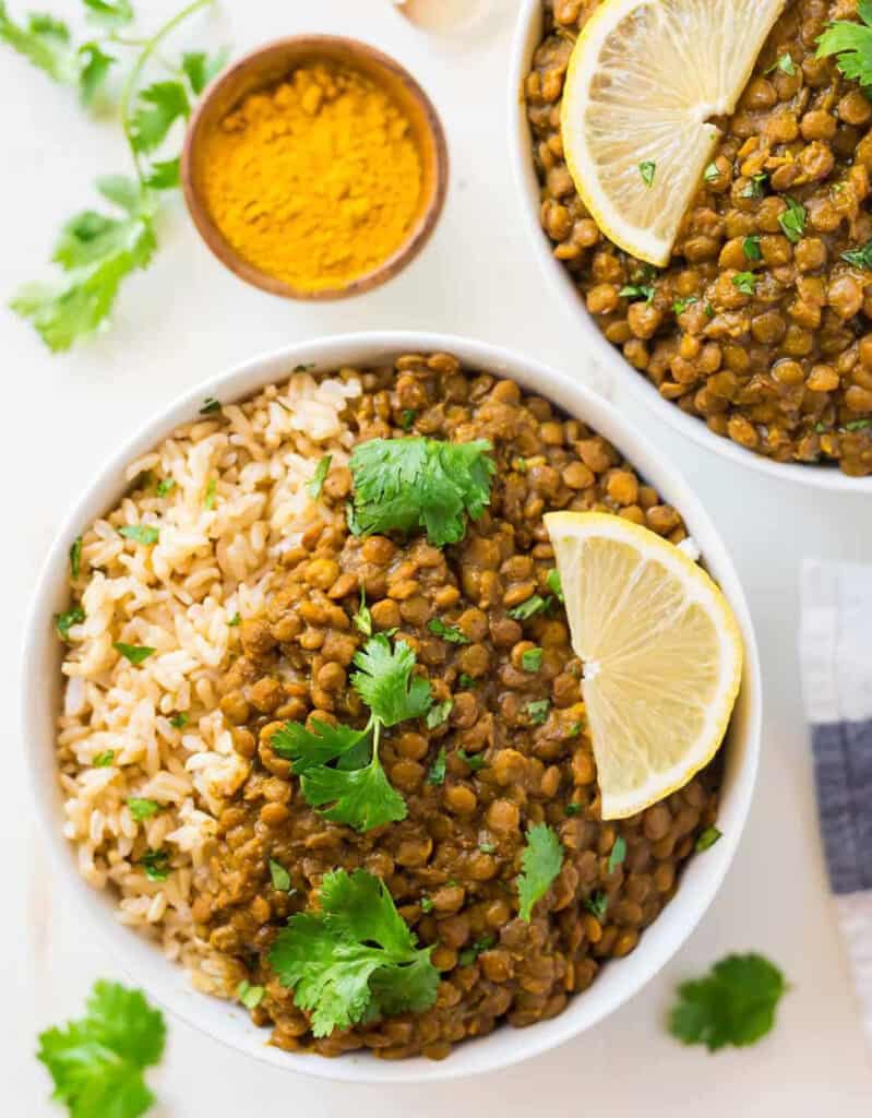 Top view of two white bowls full of rice, lentil curry, coriander leaves and a lemon wedge.