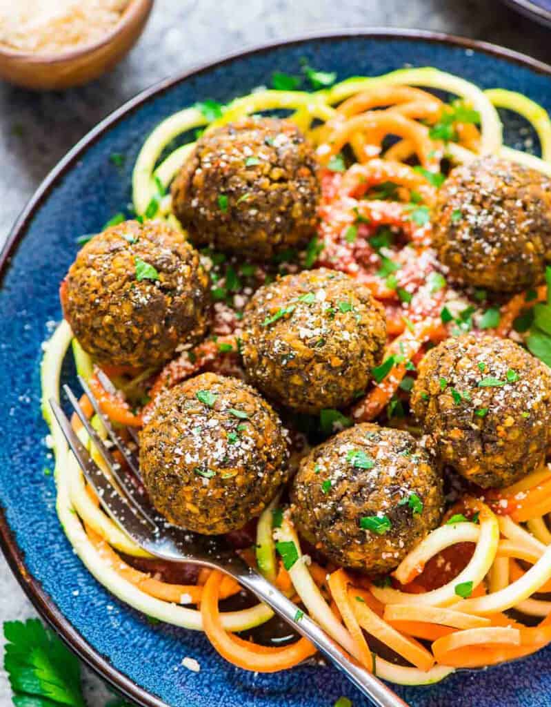 Top view of a blue plate with zoodles and lentil meatballs.