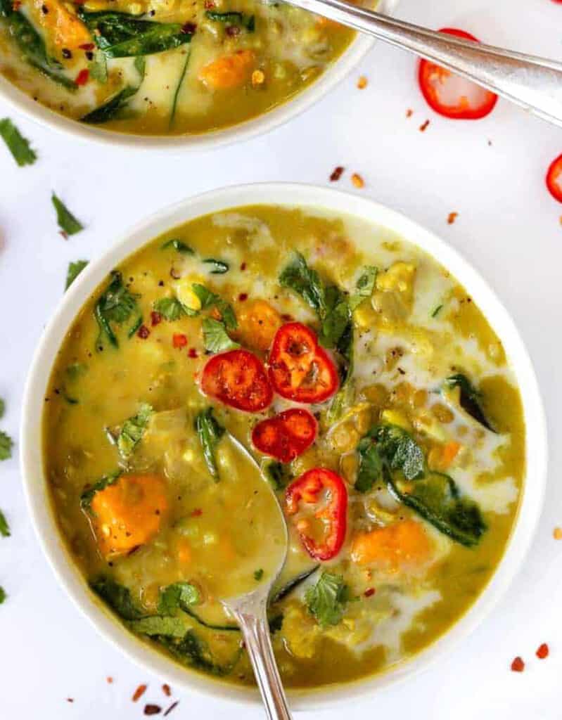 Top view of a white bowl full of green lentil soup garnished with red chili pepper slices.