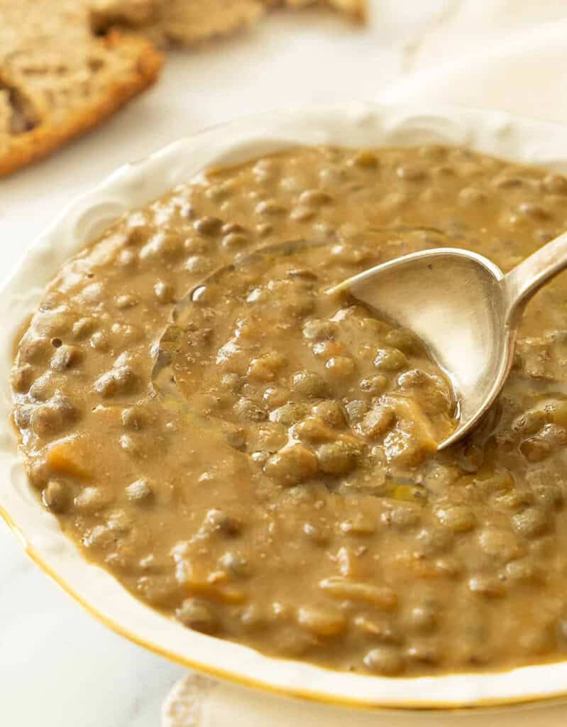 Close-up of a white bowl full of green lentil soup and a spoon.