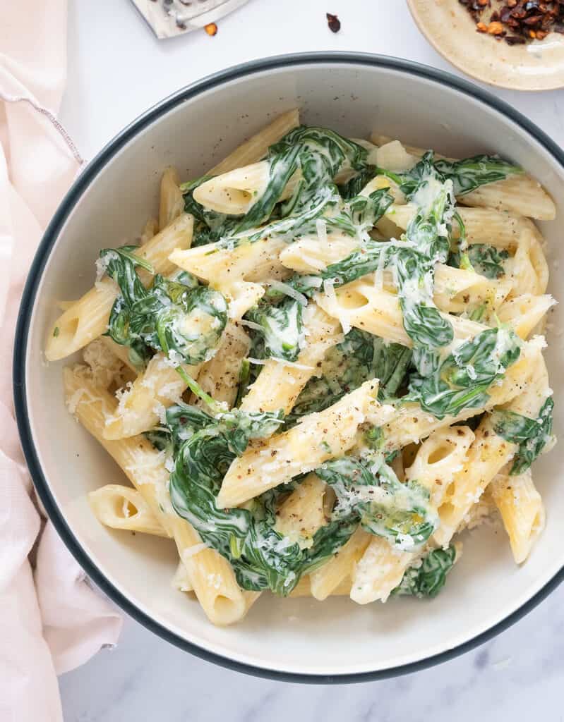 Top view of a bowl full of pasta with spinach sauce and freshly grated parmesan cheese.