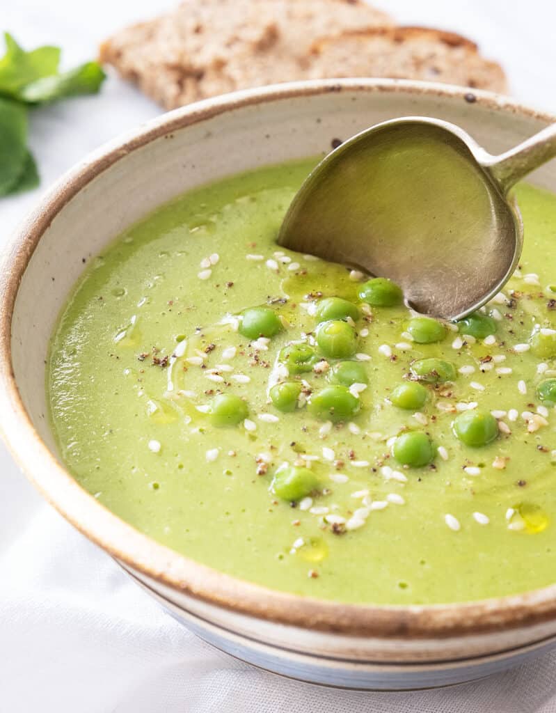 Close-up of a bowl full of pea soup with a spoon.