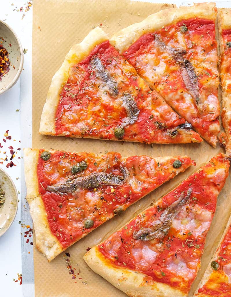 Top view of a large anchovy pizza cut into slices.