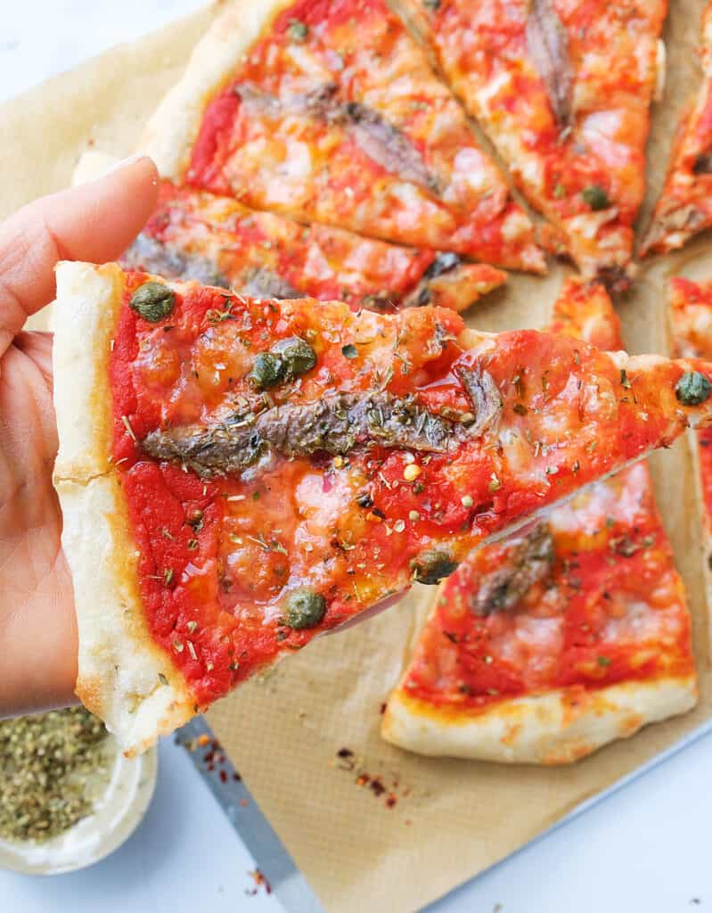 Close-up of a slice of anchovy pizza topped with anchovies, capers and oregano.