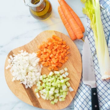 Top view of a chopping board with the soffritto ingredients: diced onion, carrots and celery.
