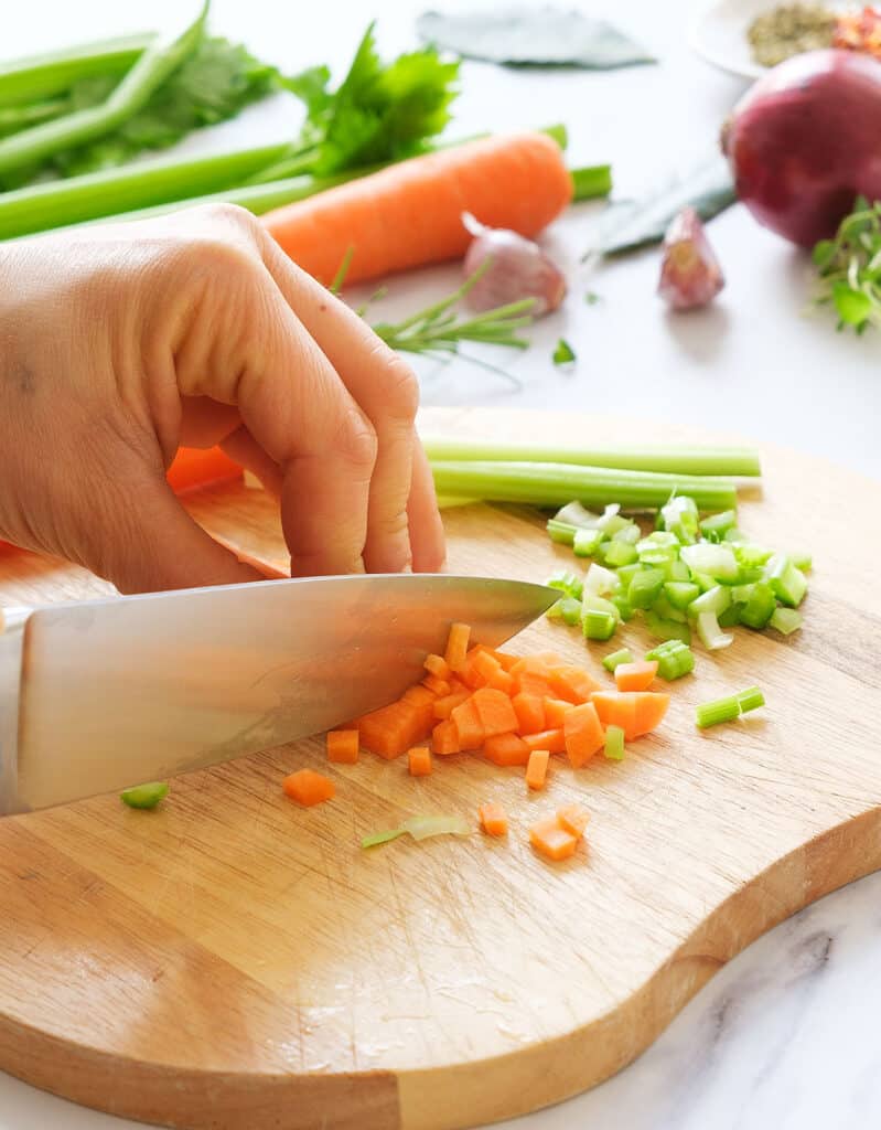 Un couteau de chef en dés de carottes et de céleri sur une planche à découper.