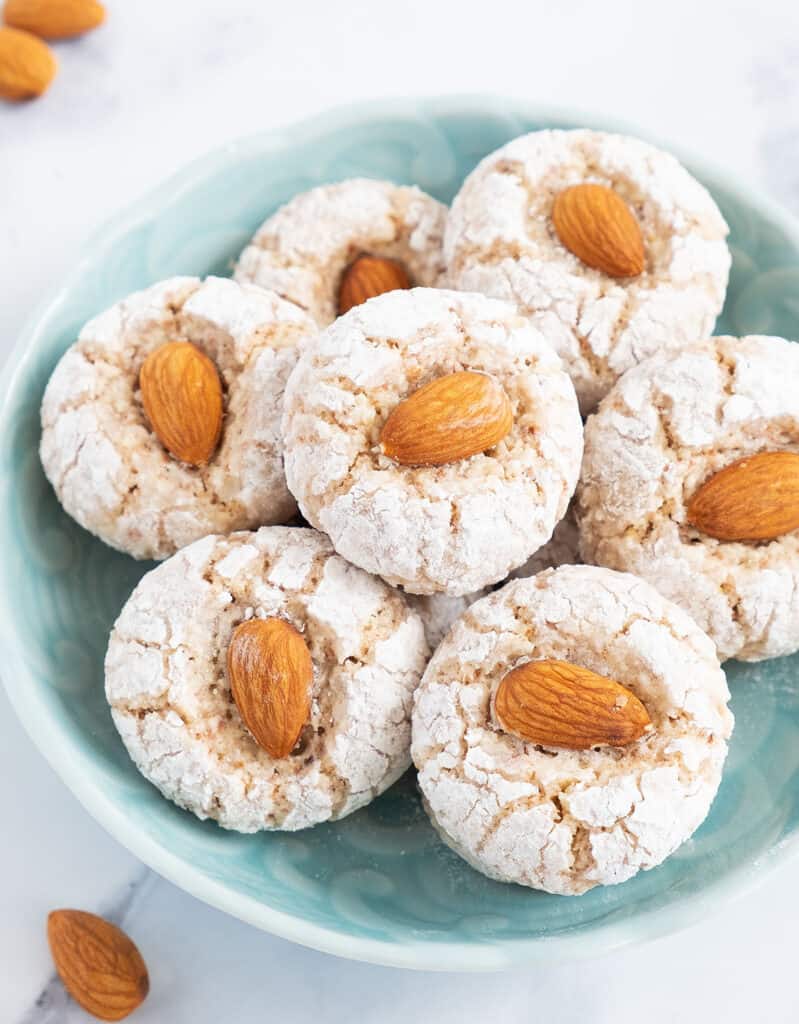 White almond cookies topped with almonds on a turquoise bowl.