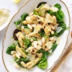 Top view of a white serving plate full of artichoke salad with greens, beans and shaved parmesan.