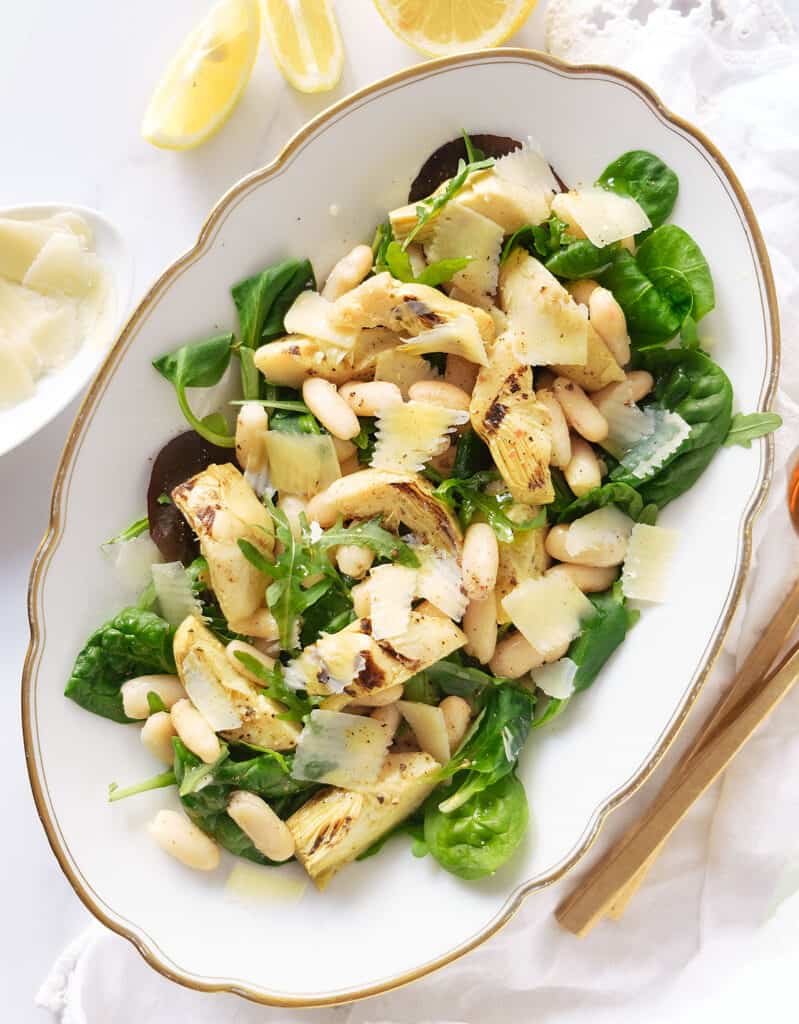 Top view of a white serving plate full of artichoke salad garnished with shaved parmesan.