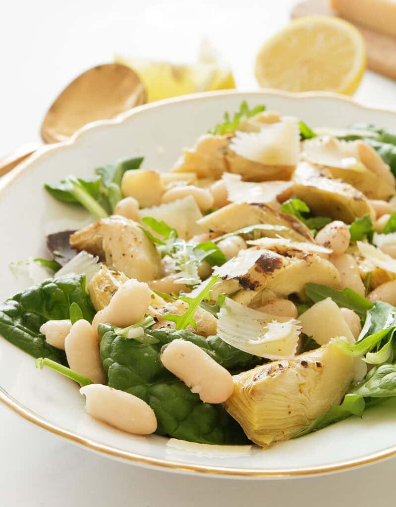 Close-up of the artichoke salad with beans and green leaves, lemon wedges in the background.