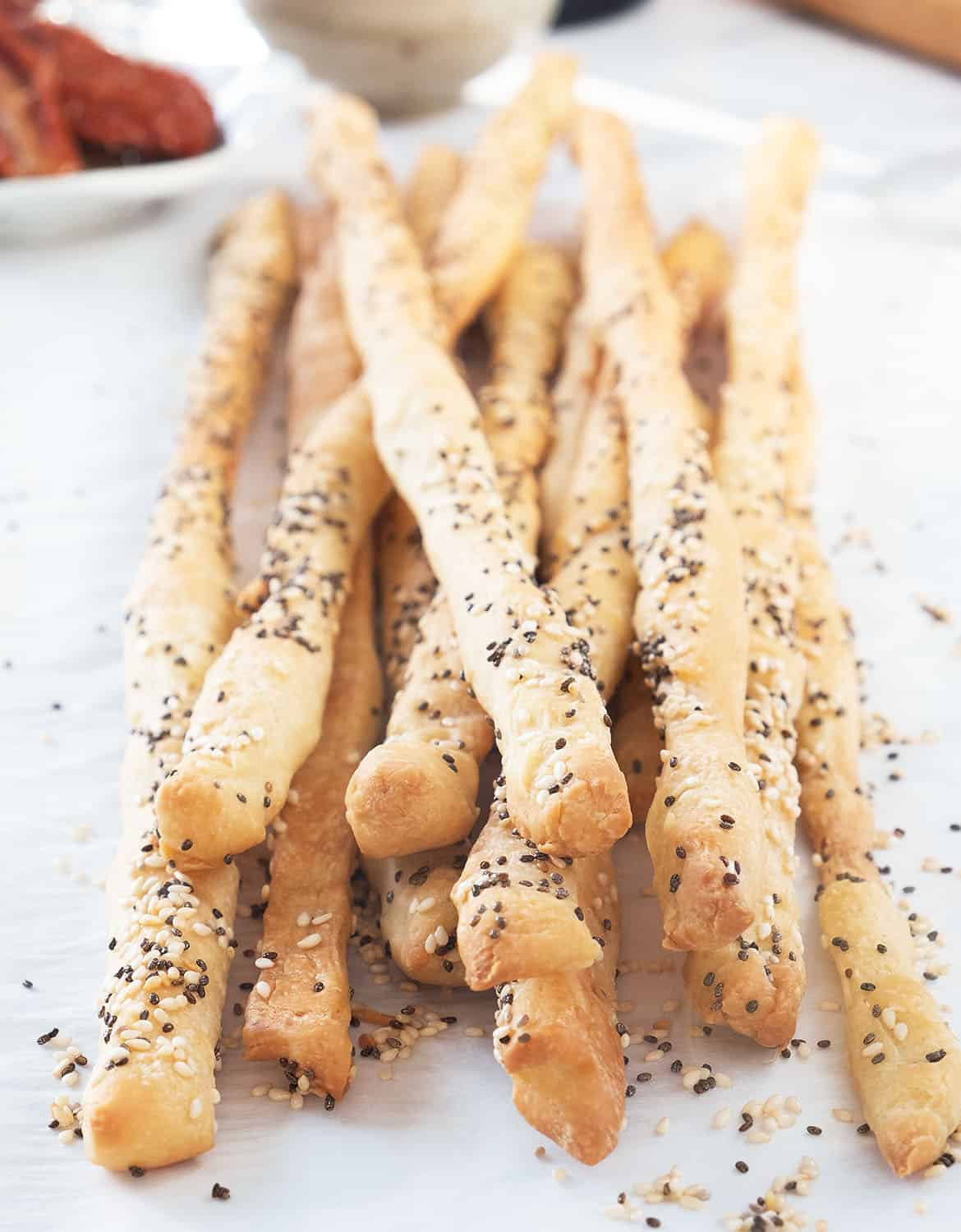 Close-up of a bunch of seeded breadsticks with a sun dried tomatoes in the background.