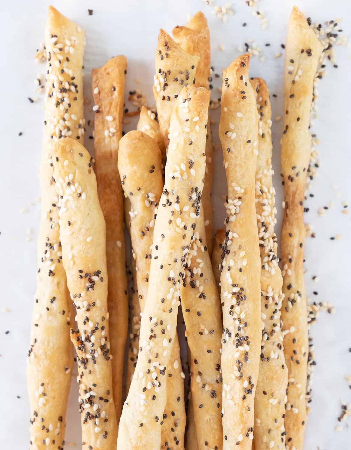 Top view of a bunch of seeded breadsticks over white parchment paper.