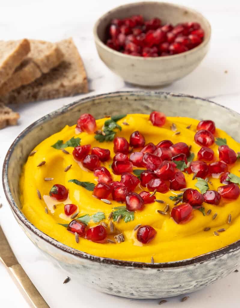 Close-up of a bowl full of carrot hummus garnished with pomegranate seeds.
