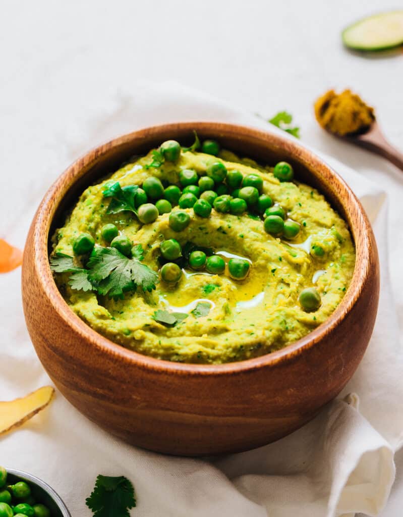 Green pea hummus in a wooden bowl over a white background.