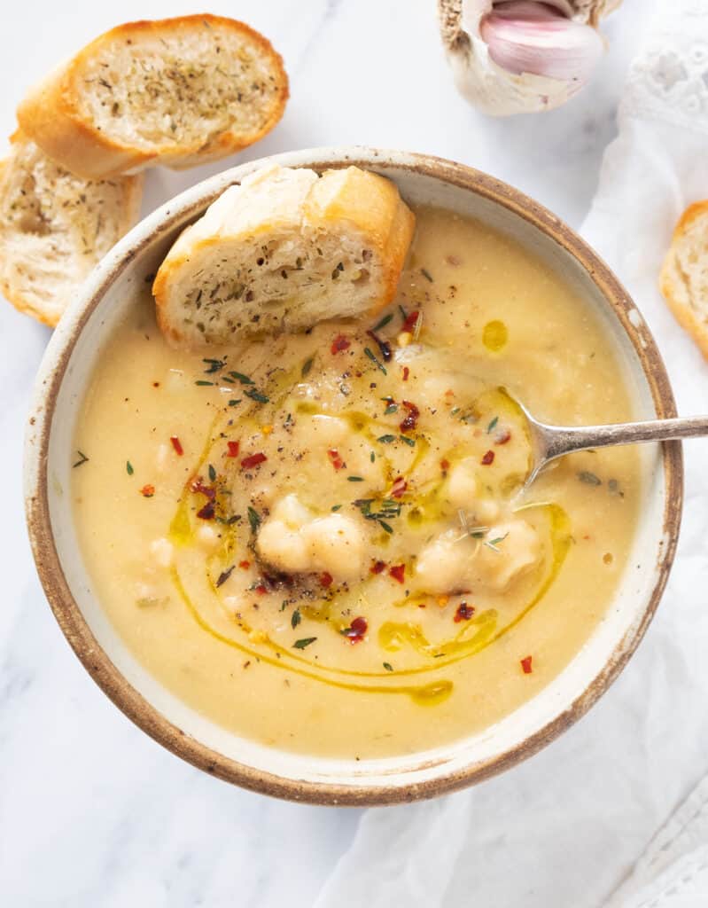 Top view of a bowl full of vegan garlic chickpea soup with a spoon served with crusty bread.