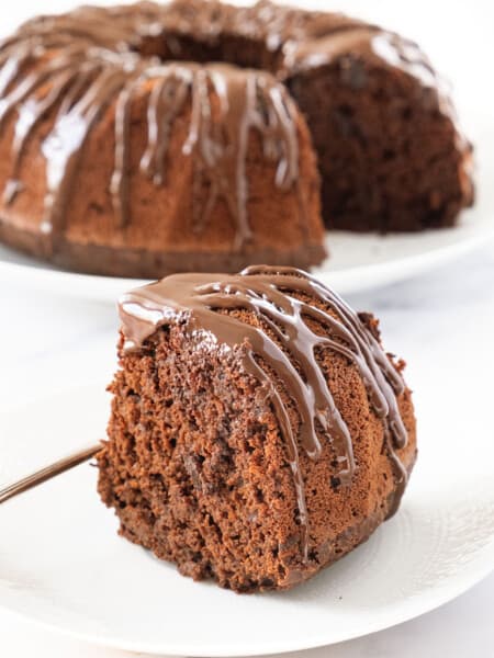 Close-up of a slice of easy chocolate cake with melted chocolate over a white background.