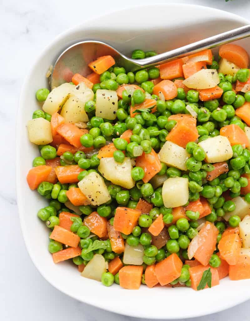Top view of a white serving dish full of peas and carrots, a classic pea recipe.