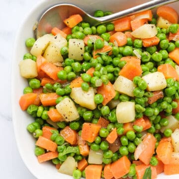 Top view of a square white serving plate with peas and carrots with cubed potatoes.