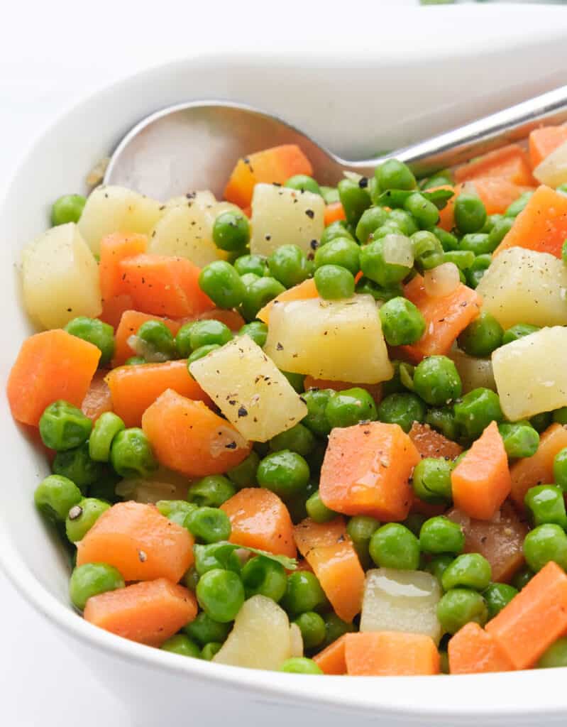 Close-up of a white serving dish with peas and carrots with cubed  potatoes.