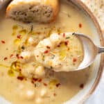 Top view of a bowl full of vegan garlic chickpea soup with a spoon.