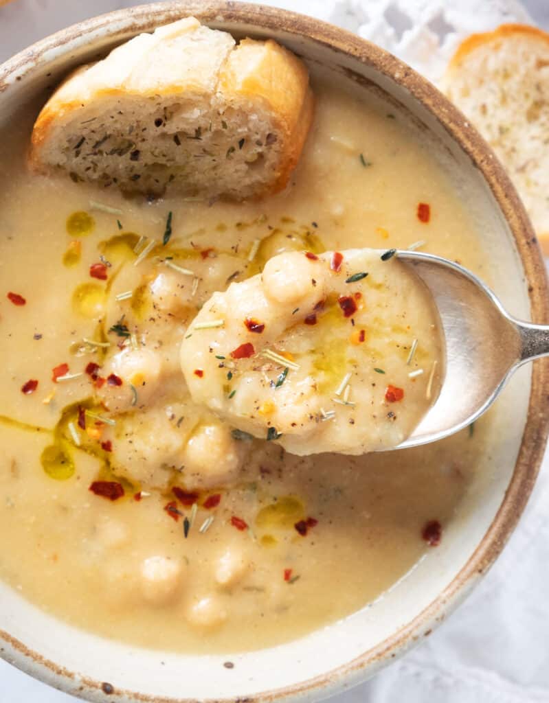 Top view of a bowl and a spoon full of garlic chickpea soup with chili flakes and dried herbs.