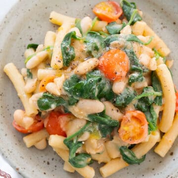 Top view of a grey plate full of white bean pasta with spinach and cherry tomatoes.