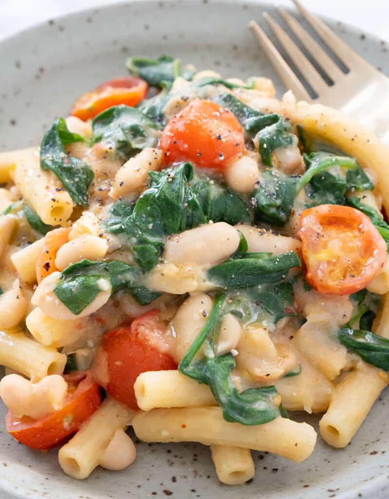 A grey plate full of one-pot white bean pasta with spinach and cherry tomatoes.
