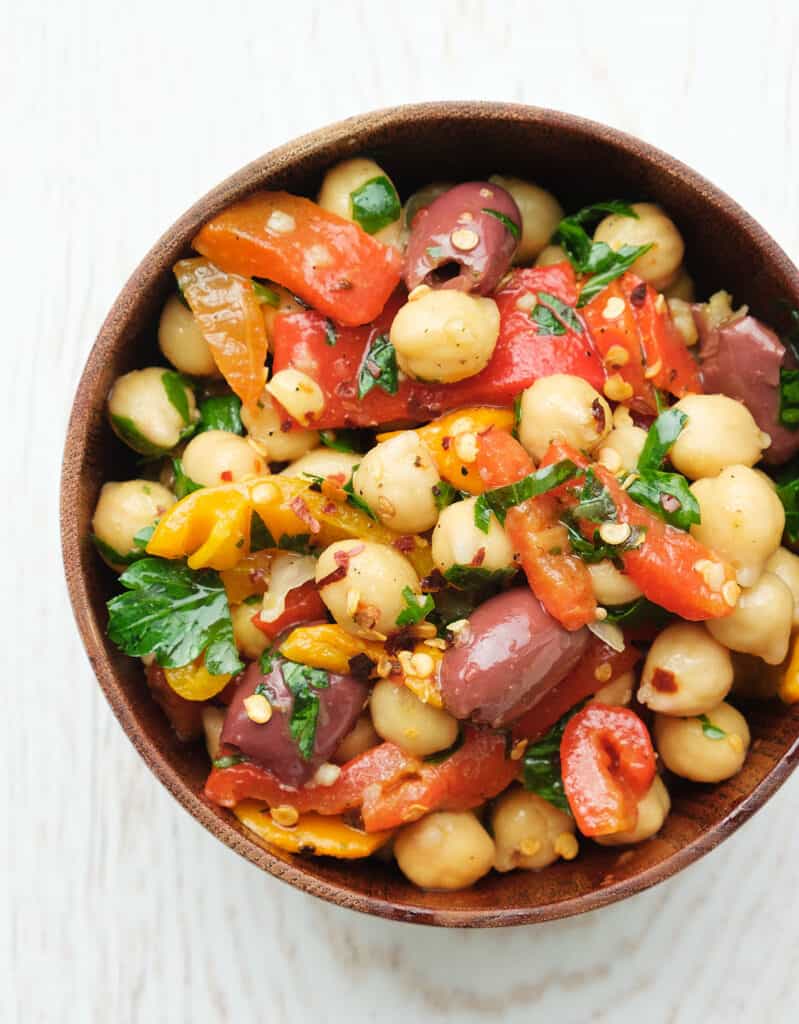 Top view of a bowl full of chickpea salad with peppers and olives over a white background.