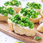 Close-up of a crostini with ricotta and peas on a small wooden board.