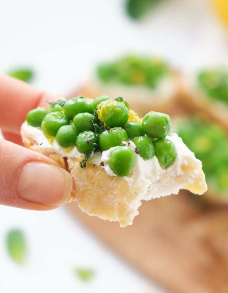 Close-up of a hand holding crostini with ricotta and peas.