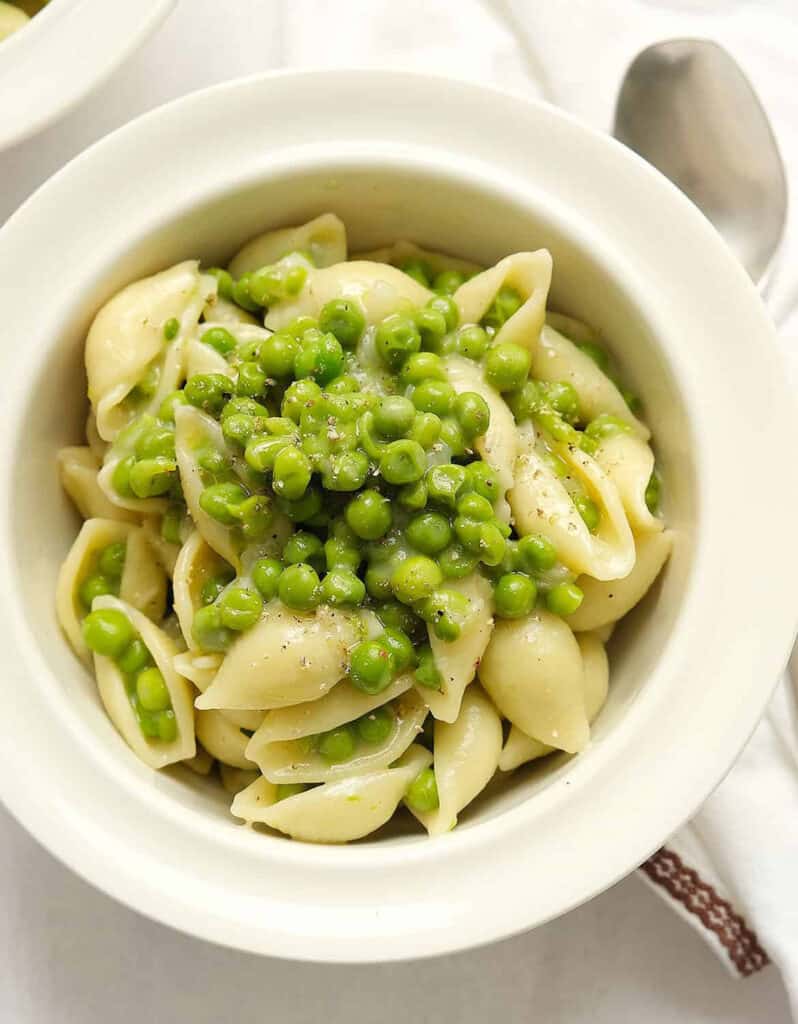 Top view of a white bowl full of one-pot pasta with peas over a white background.