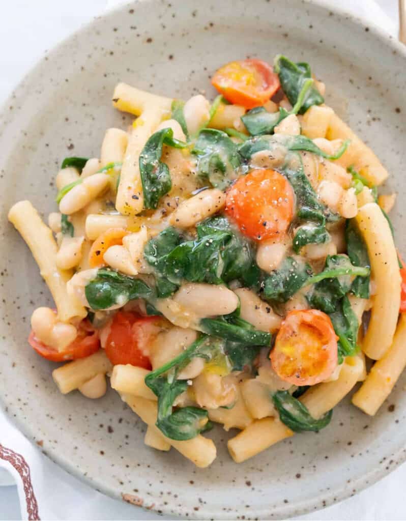 Top view of a grey dish full of one-pot white bean pasta with spinach and cherry tomatoes.