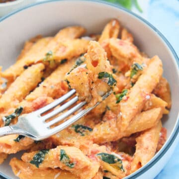 Close-up of a fork lifting some penne pasta with tomato basil sauce.