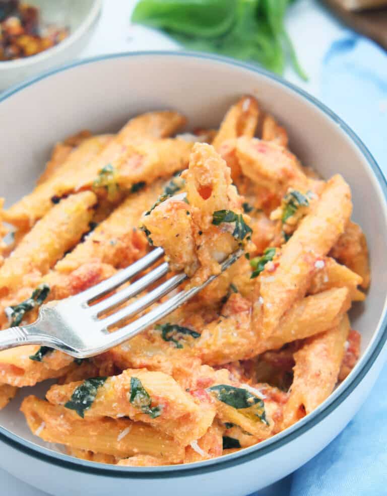 Close-up of a fork lifting some penne pasta with tomato basil sauce.