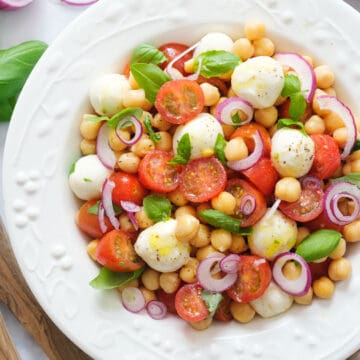 Top view of a white plate full of Italian chickpea salad with cherry tomatoes, mozzarella and basil.