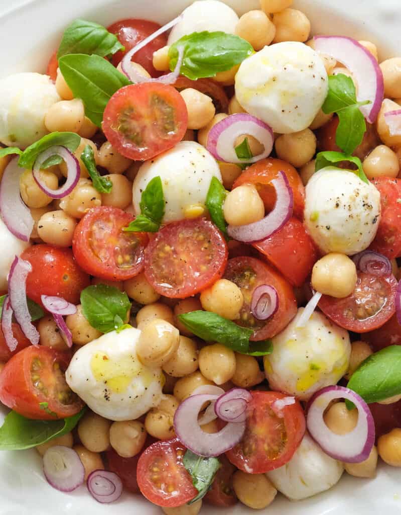 Close-up of a large portion of Italian chickpea salad with mozzarella, cherry tomatoes and basil leaves.