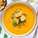 Top view of a bowl full of creamy carrot and ginger soup garnished with coriander and croutons.