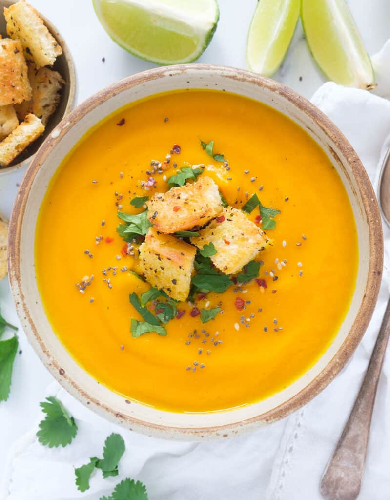 Top view of a bowl full of creamy carrot ginger soup garnished with croutons and fresh coriander.