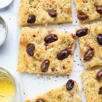 Top view of easy focaccia with olives cut into slices over a white background.