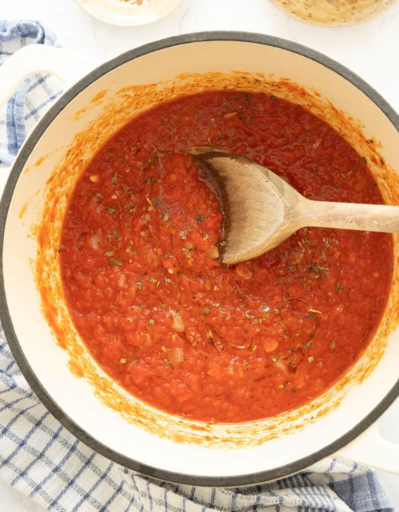 Top view of a pot full of marinara sauce with a wooden spoon.