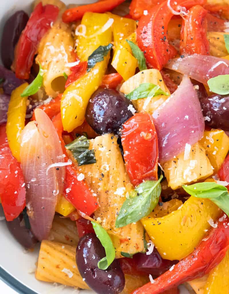 Close-up of some pasta with peppers, with fresh basil leaves and some parmesan cheese.