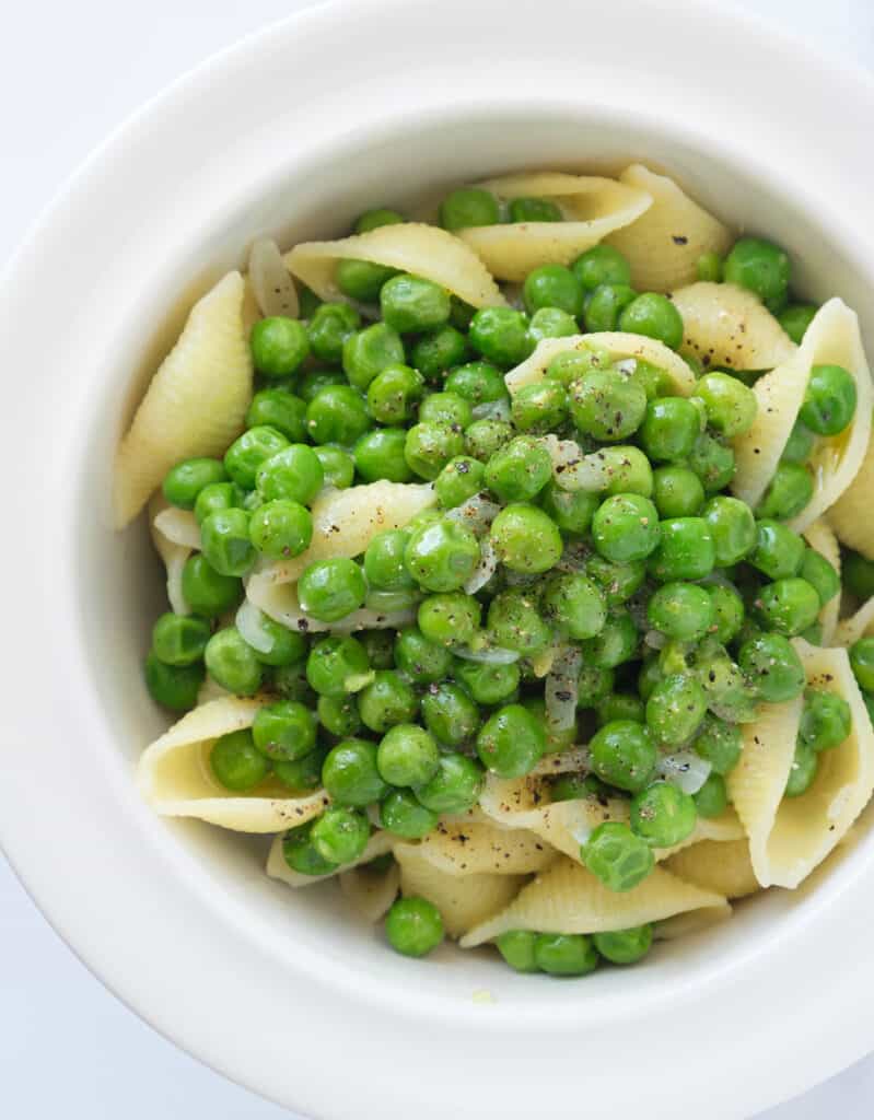 Top view of a white bowl full of pasta with peas. 