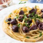 Close-up of a white plate full of pasta with olives.