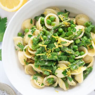 Top view of a white bowl full of peas and asparagus pasta.