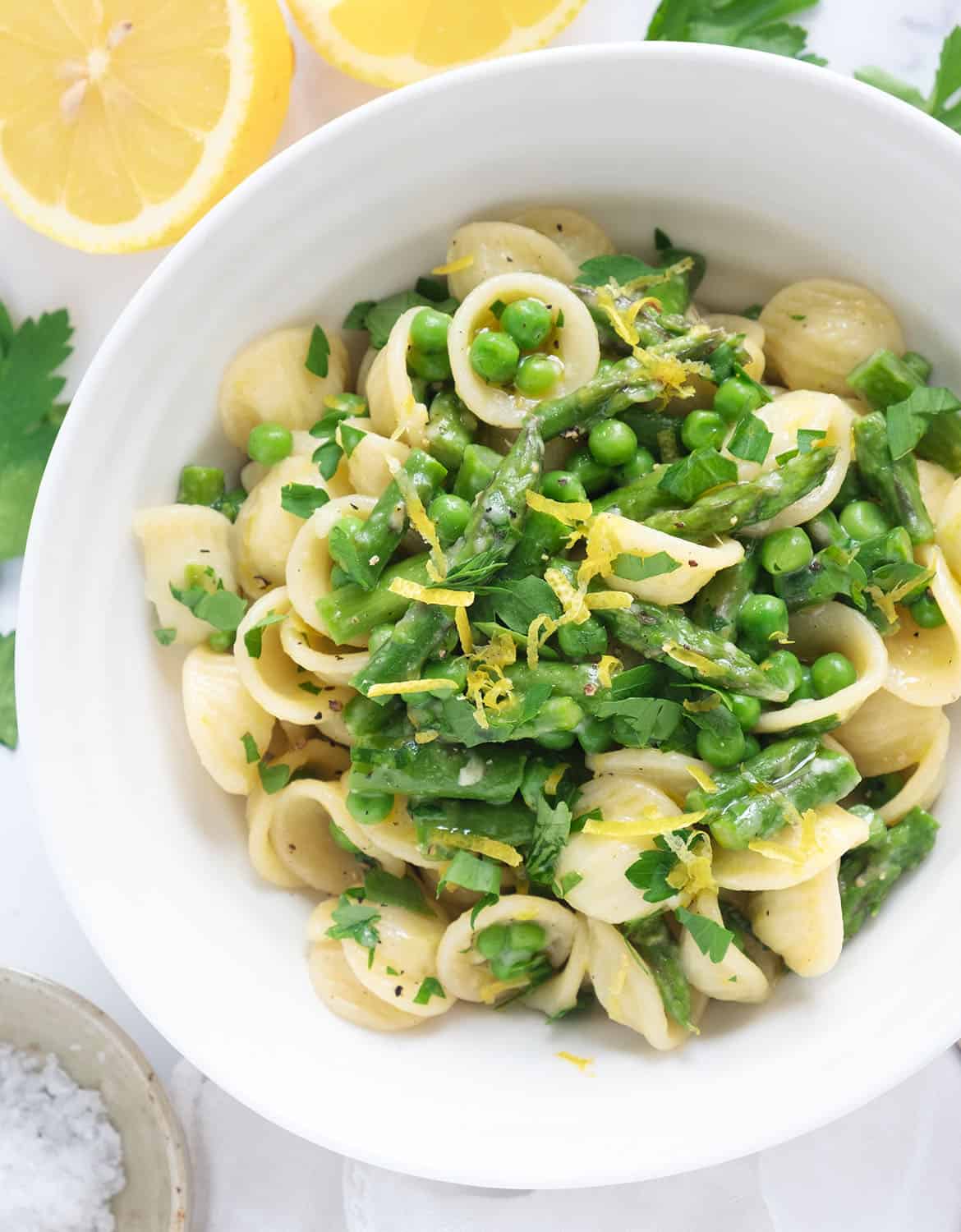 Top view of a white bowl full of pasta with peas and asparagus.