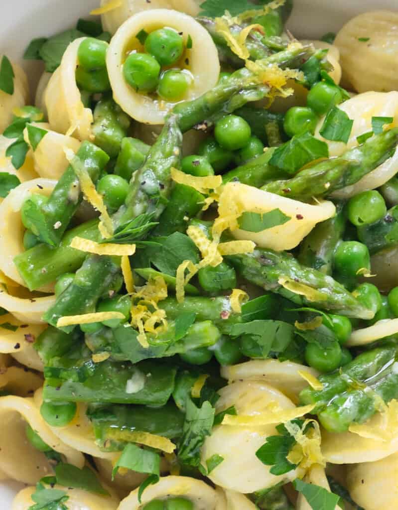 Close-up of a plate full of pea and asparagus pasta with lemon zest.