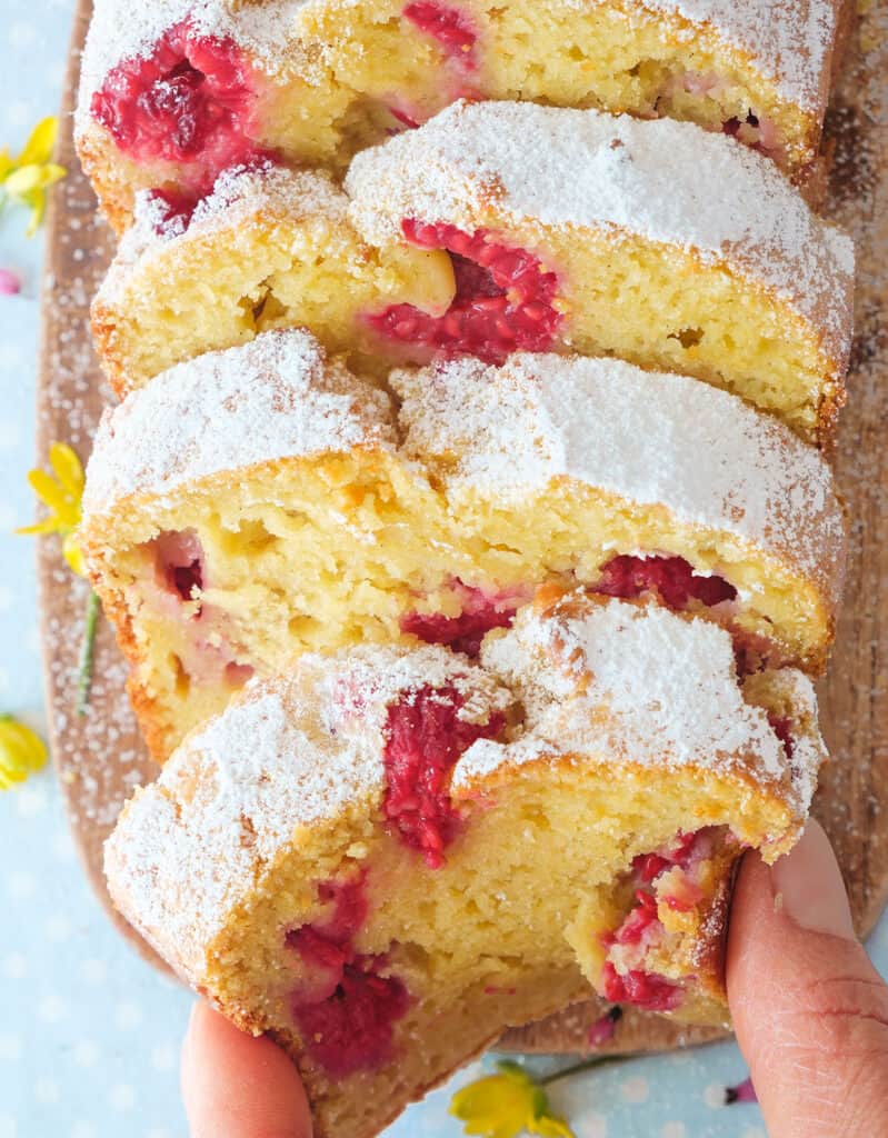 A hand grabbing a soft and moist slice of raspberry ricotta cake.