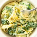 Top view of a white bowl full of spaghetti with ricotta sauce and spinach.